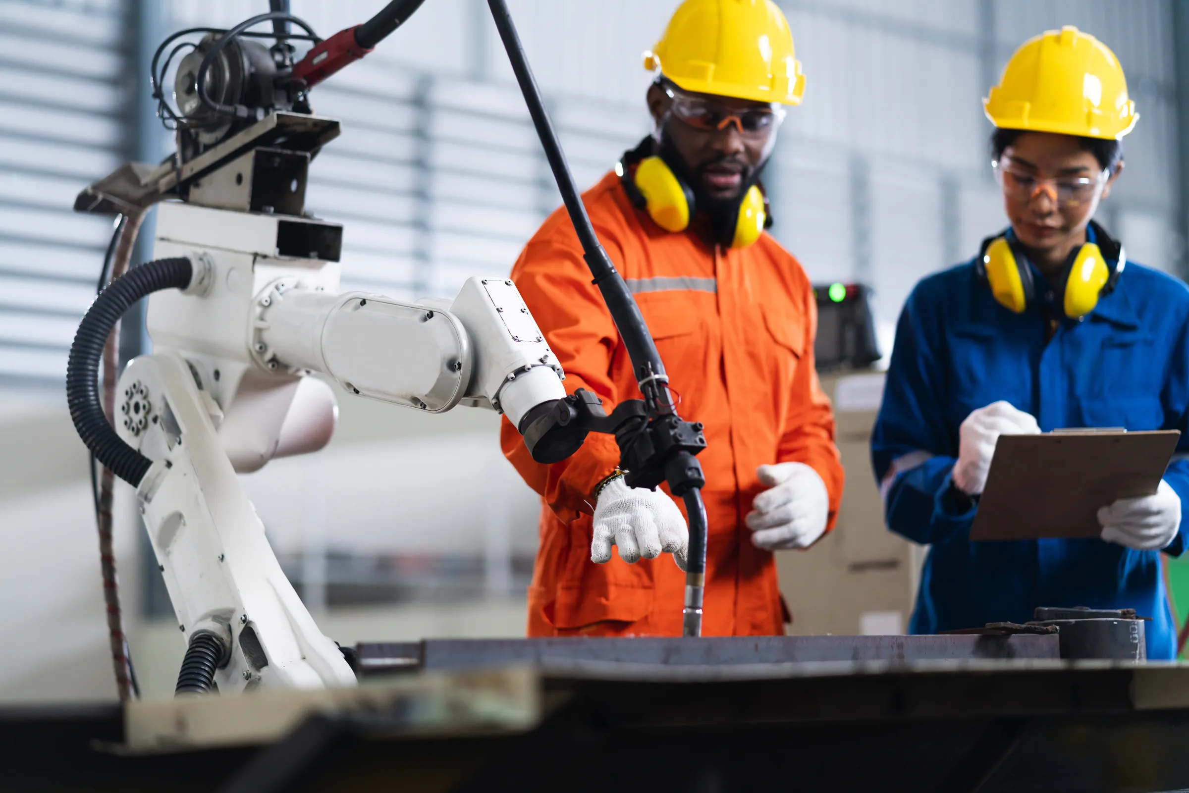 Dois profissionais de segurança inspecionando um braço robótico industrial com prancheta