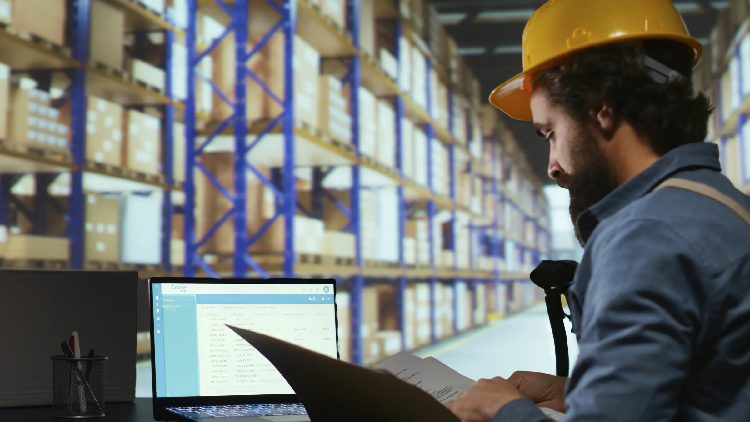 Profissional revisando documentos e checklist em notebook dentro de um armazém industrial